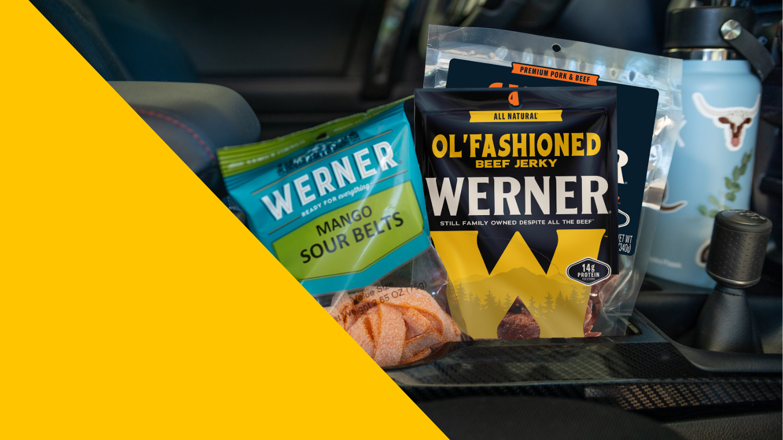 Packaged snacks including Werner beef jerky and Sour Belts in a car center console.