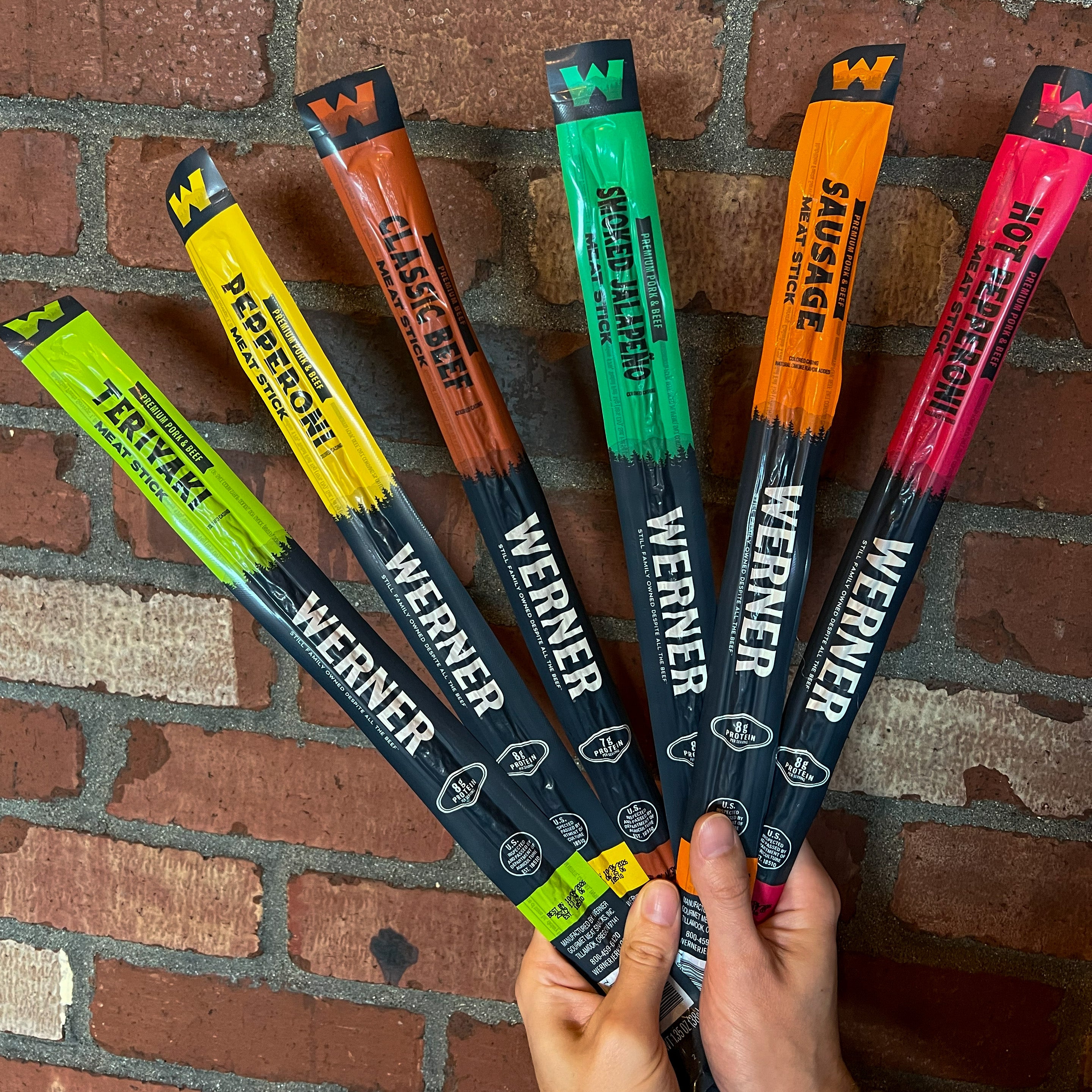 a hand holding multiple meat sticks of varying colors